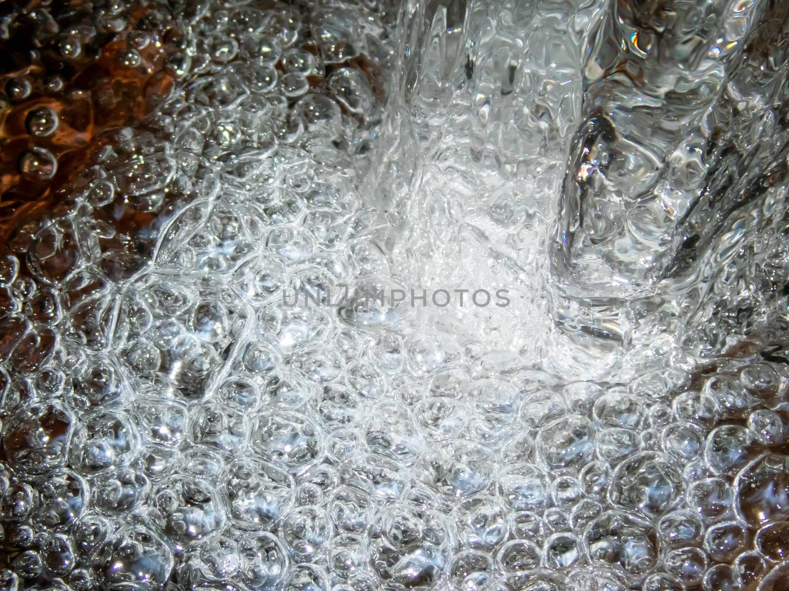 Dynamic energy in a whirl of splashing bubbles at the base of a rock where water pours over into a flowing stream. No people with copy space, shot outdoors in natural light.