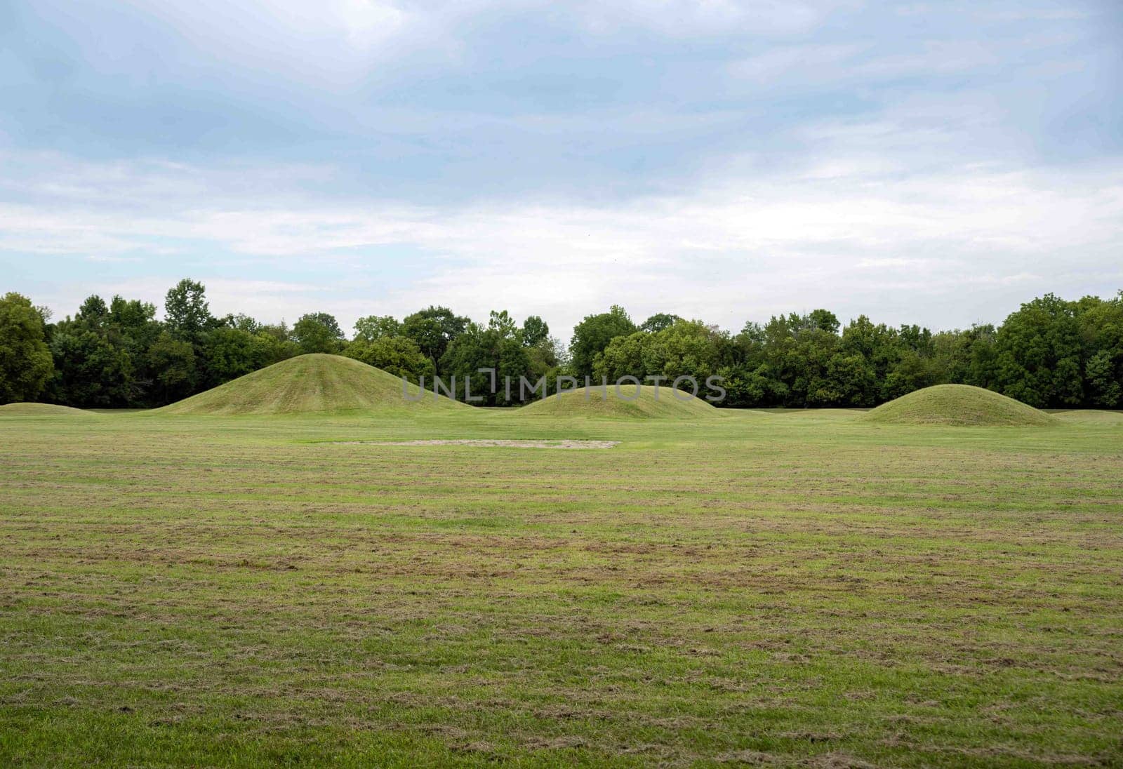 Native American Hopewell Culture prehistoric Earthworks burial mounds in Mound City park Ohio. Ancient circular mounds and long mounds in a row. Grass is neatly trimmed with trees and dramatic sky.