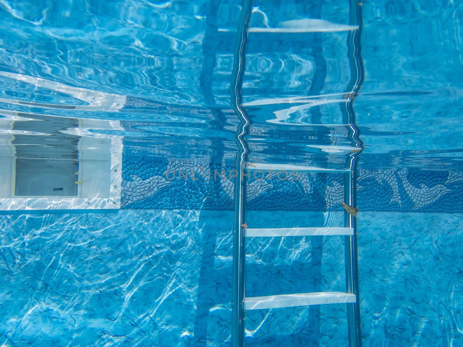 Beautiful clean blue water and decorative pool liner with ladder and skimmer pool equipment underwater camera captures tranquil scene with reflection. Copy space, no people, shot outdoors in natural light.