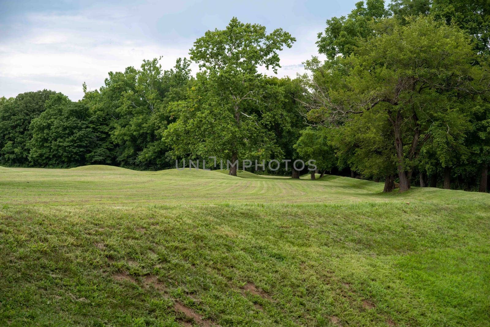 Native American Hopewell Culture prehistoric Earthworks burial mounds in Mound City park Ohio. Ancient small circular mounds with a long mound surrounding. Grass is neatly trimmed with trees and dramatic sky.