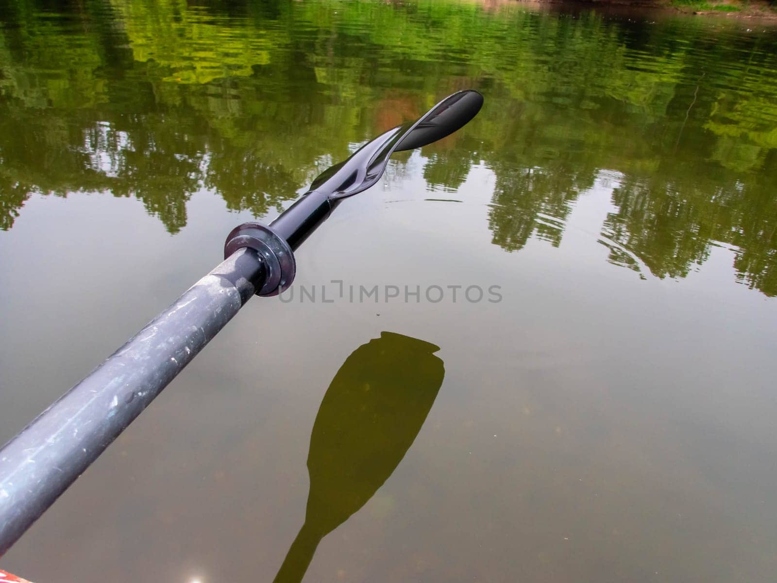 Adventure river scene with raised paddle oar and smooth watr surface with woodland riverbank reflected