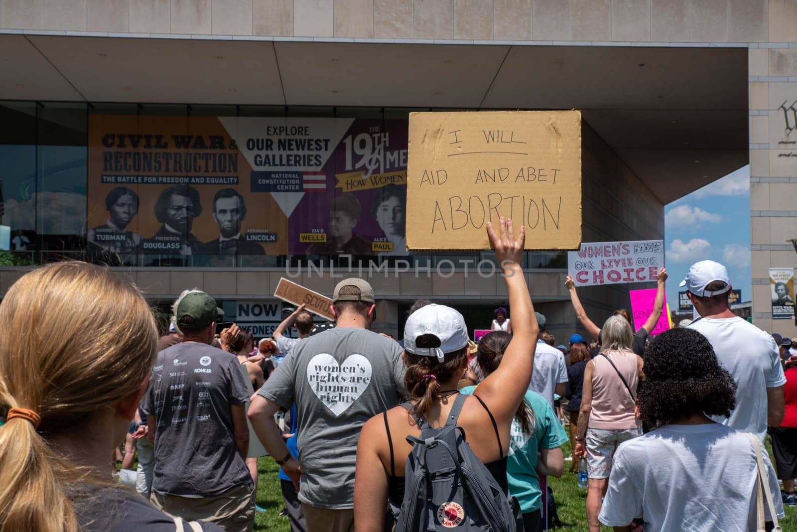 Philadelphia, PA  USA - 06-25-2022 National Constitution Center, a young woman in a crowd holds up a sign I WILL AID AND ABET ABORTION at an outdoor political pro-choice Josh Shapiro for governor rally