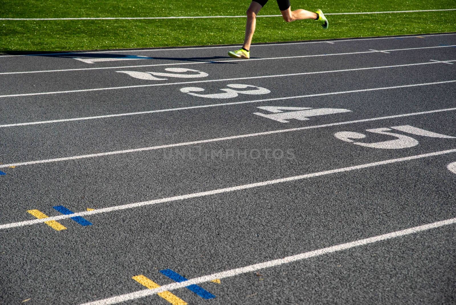 A runner on a gray athletic running track with large white numbers. Runner races over numbers with copy space. Selective focus on track for excellent track and field background.