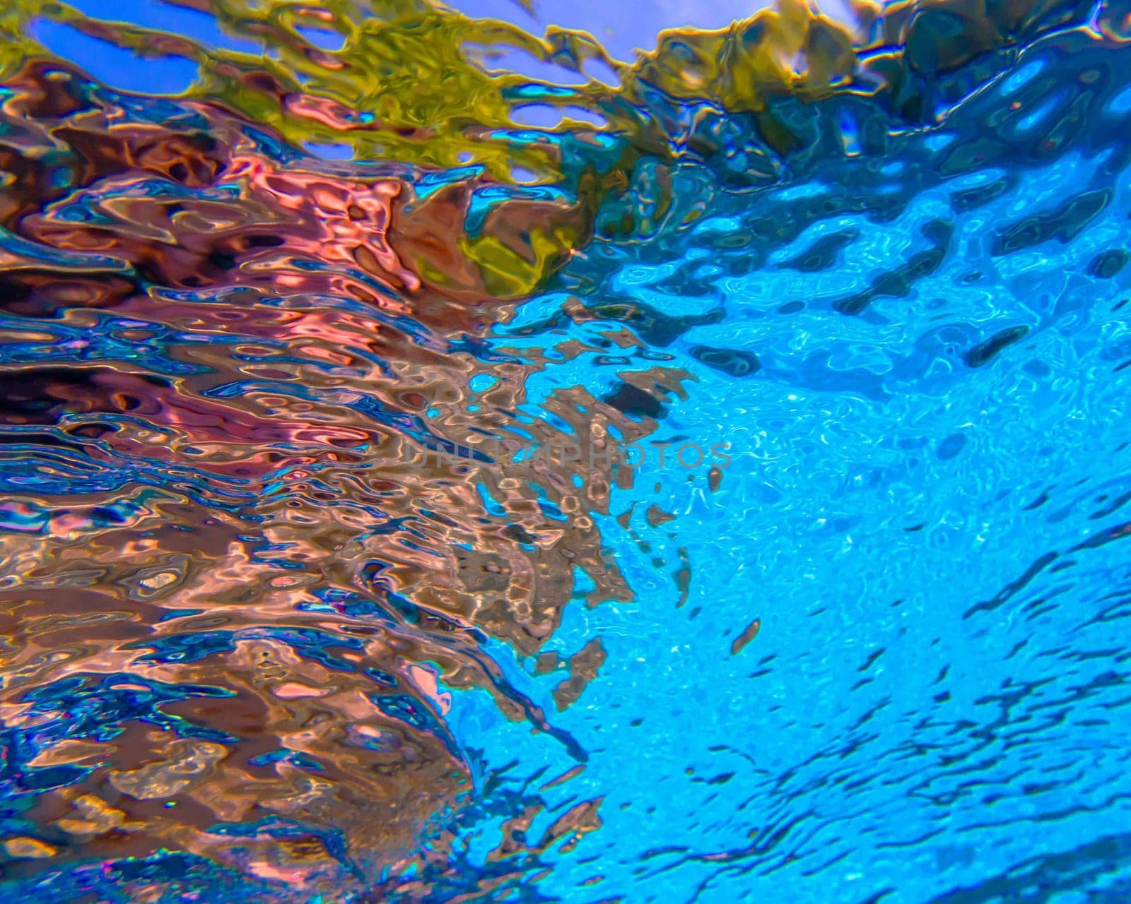 Beautiful underwater shot looking up through the surface of a swimmming pool. Excellent background with abstract colorful eye-catching dynamics. No people and plenty of copy space.