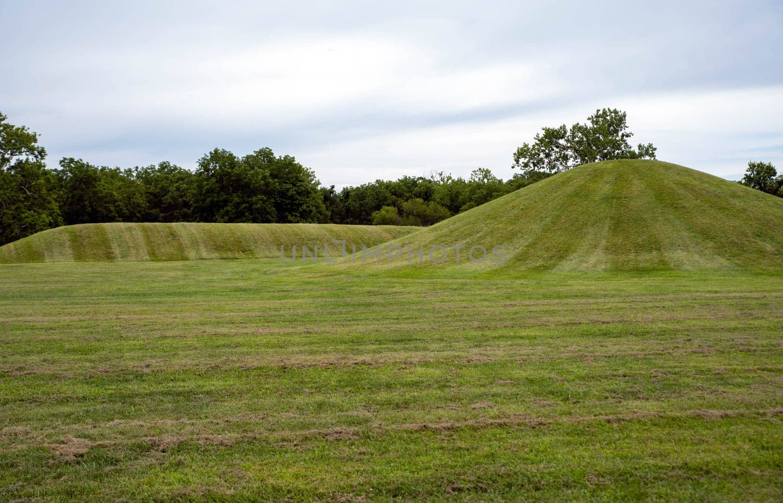 Mound City ancient Hopewell Culture burial mounds, one circular and one long covered in neatly trimmed grass under a dramatic sky
