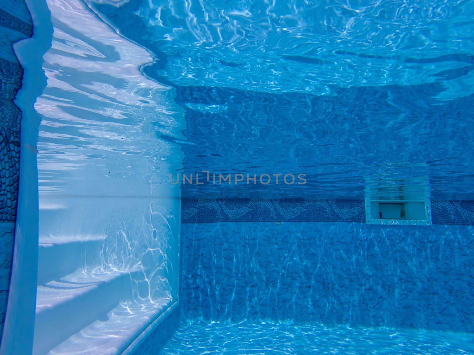 Serene relaxing view of pool steps and dappled light rippling on walls and floor, Blue design on walls taken with an underwater camera. Underside of water surface relects pool bottom.