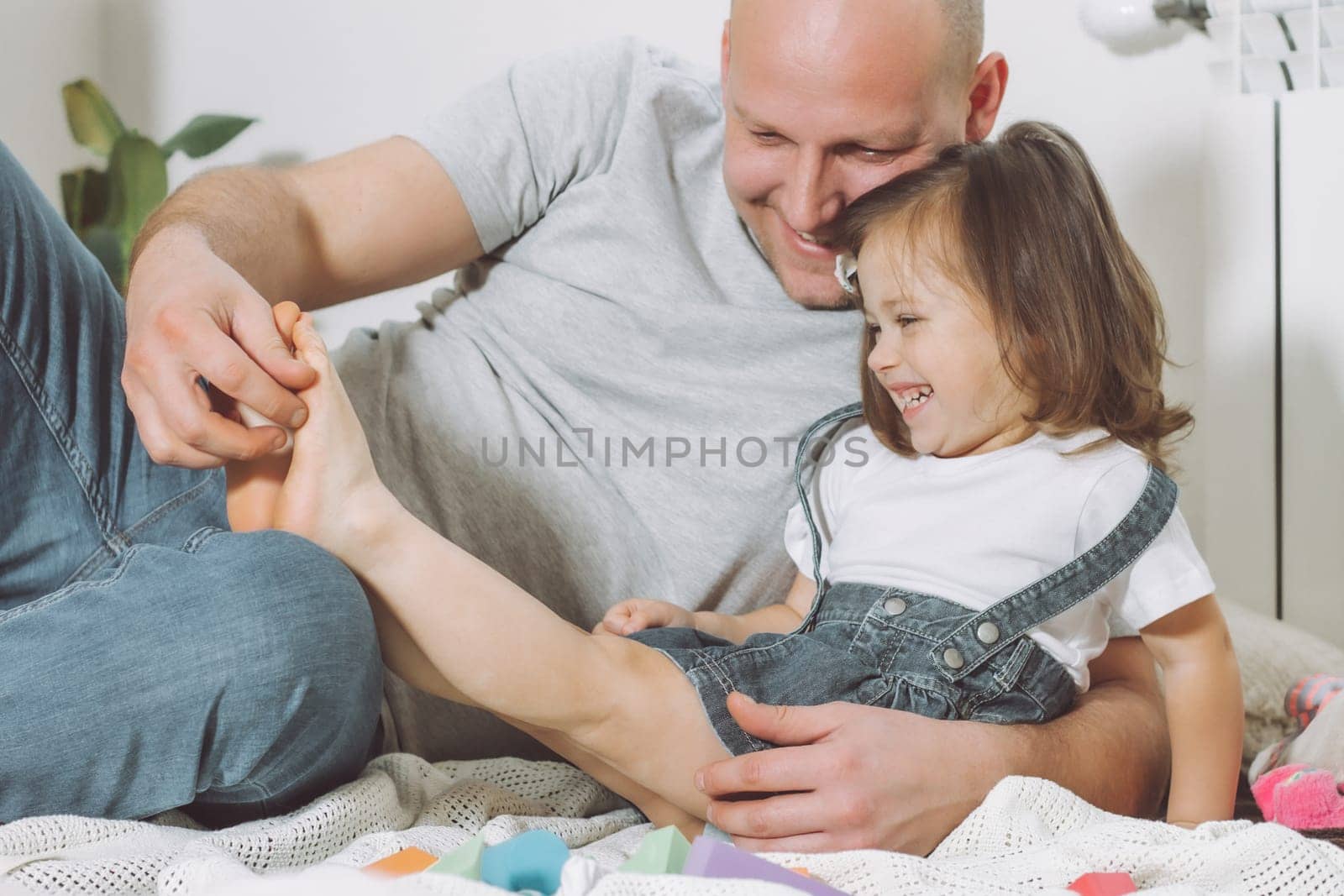 Father plays with little daughter 2-4 on floor. Dad tickles kids feet. Family, having fun