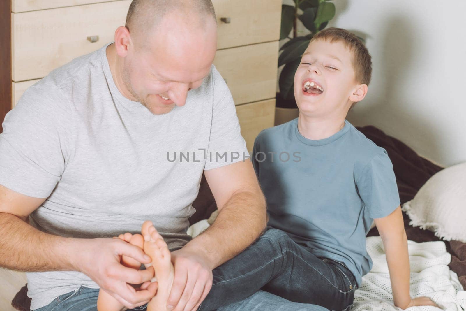 Father plays with his son 7-10 sitting on floor. Dad tickles kids feet. Family having fun