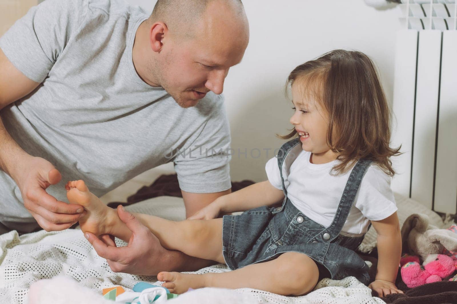 Father plays with little daughter 2-4 on floor. Dad tickles kids feet. Family, having fun
