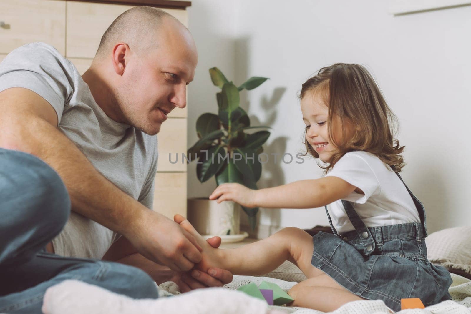 Father plays with little daughter 2-4 on floor. Dad tickles kids feet. Family, having fun