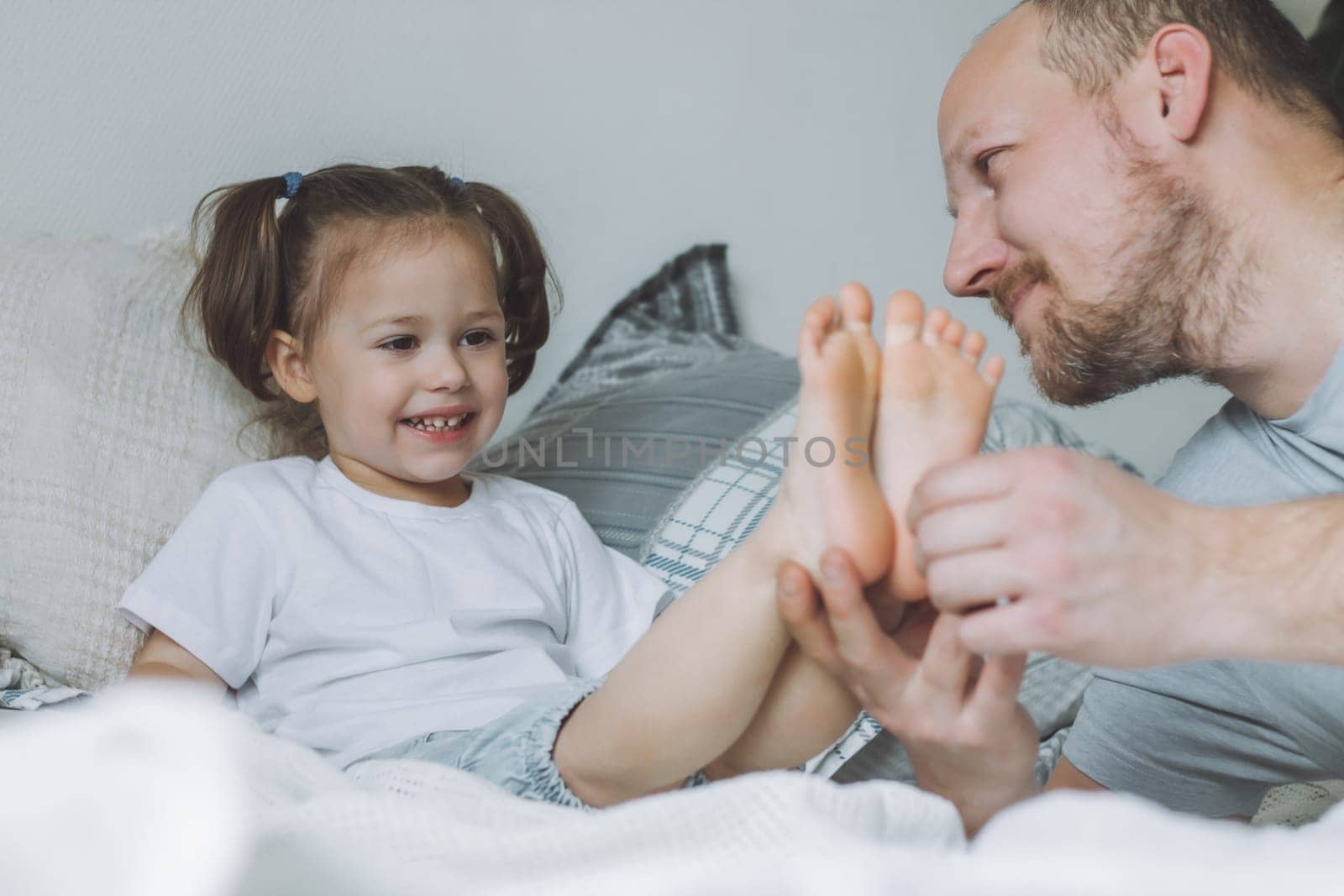 Father plays with little daughter 2-4 on bed. Dad tickles kids feet. Family having fun