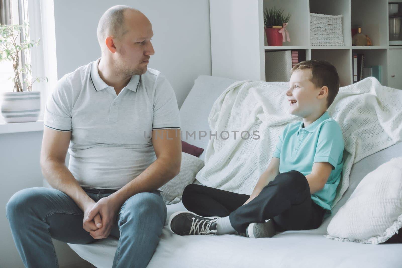 Dad and son sitting on couch, talking to each other and smiling