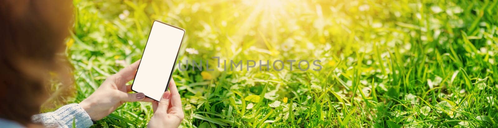 Woman holding in her hands smartphone with mockup screen. Panoramic view of the blossoming natural park.