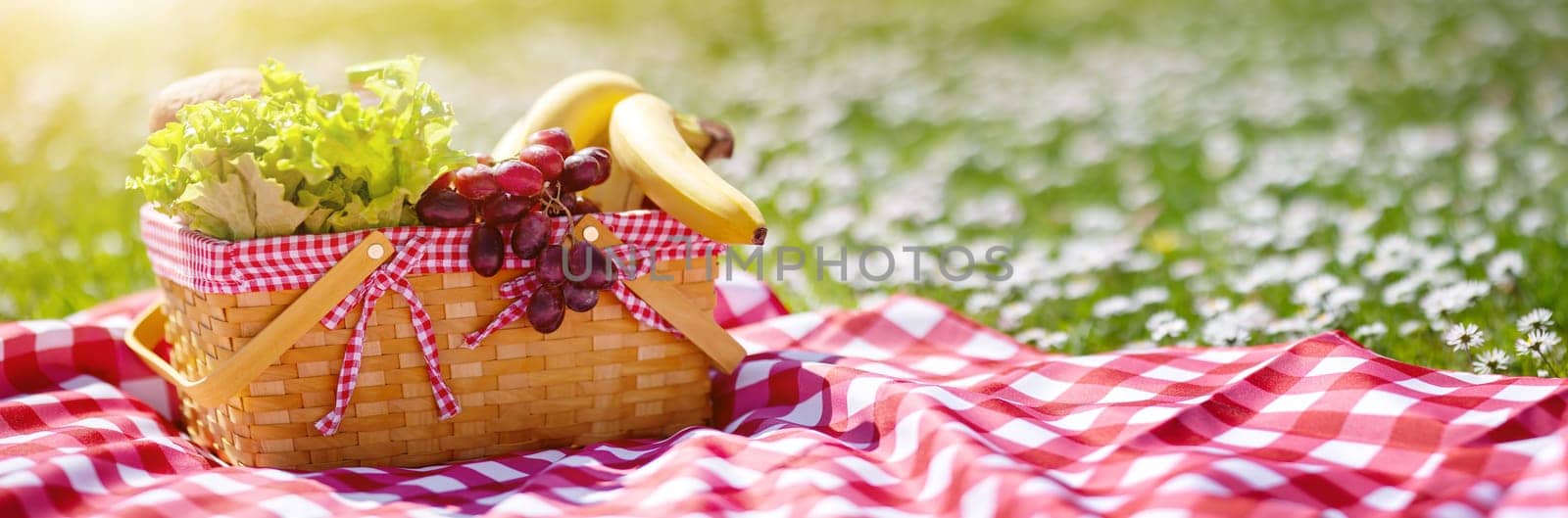 Wicker basket with food standing on the picnic blanket in nature. Concept of the family weekend and romantic picnic.