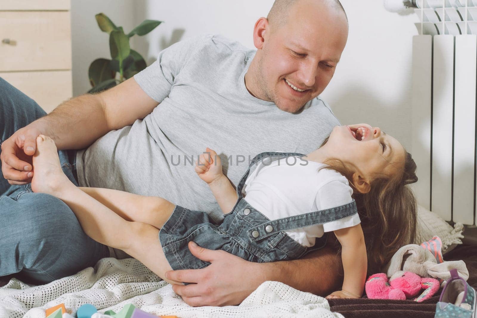 Father plays with little daughter 2-4 on floor. Dad tickles kids feet. Family, having fun