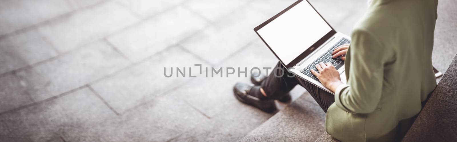 Young woman with laptop sitting on the stairs. Person using personal computer outdoors.