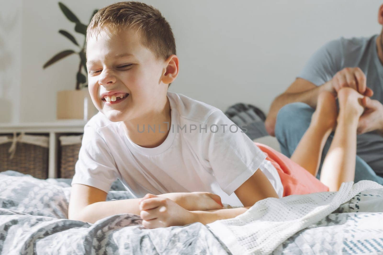Father plays with his son 7-10 on bed. Dad tickles kids feet. Family having fun