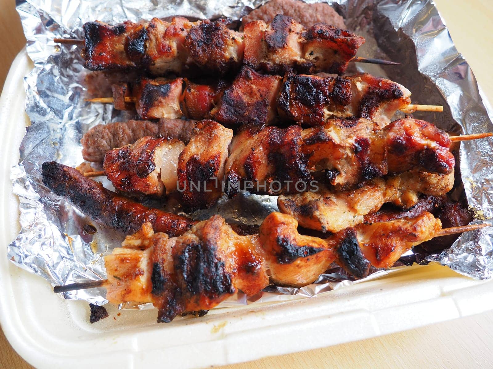 Grilled meat in disposable packaging and aluminum foil, delivered from a restaurant. Food delivery home from restaurants and cafes. Shish kebab and lumpy meat of chicken, pork and lamb.