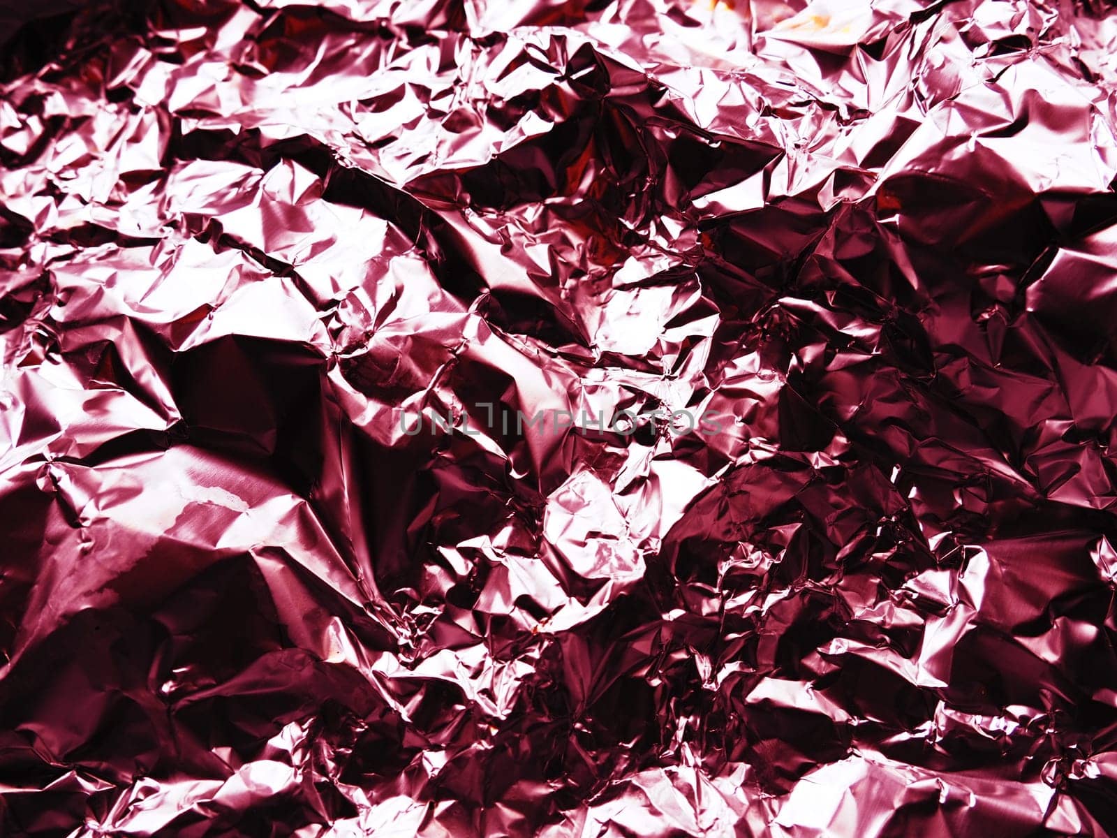 foil close-up. Aluminum silver crumpled foil. Abstract metallic background. Foil for baking food. Background with a red or burgundy tint.