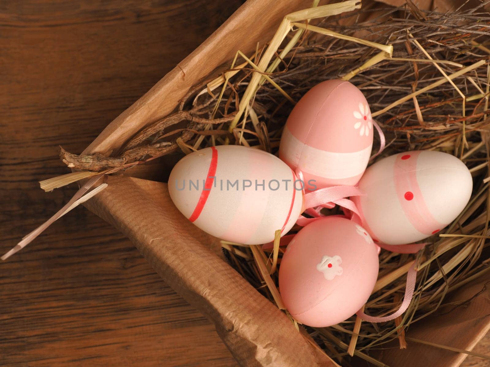 Pink Easter eggs in a cardboard box on a rustic wooden table background with space for text