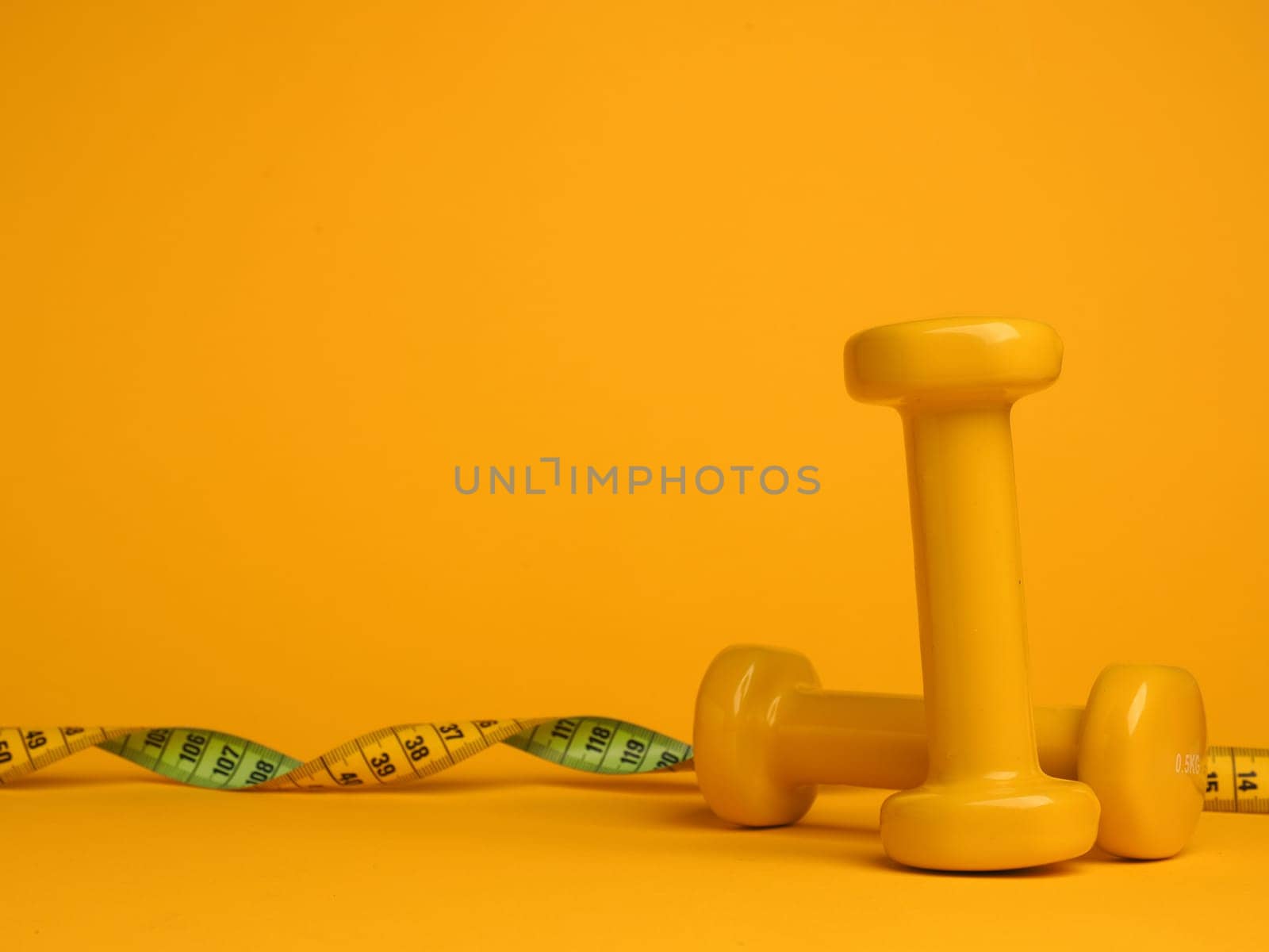 Yellow dumbbells with a tape measure on a yellow background, space for your text, fitness or diet concept
