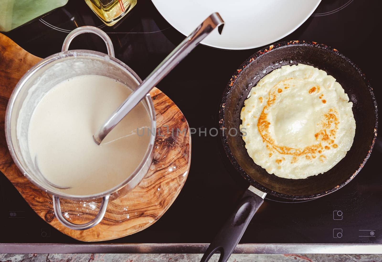 Making thin pancakes on frying pan in kitchen, with cooking dough for crepes and pancakes.