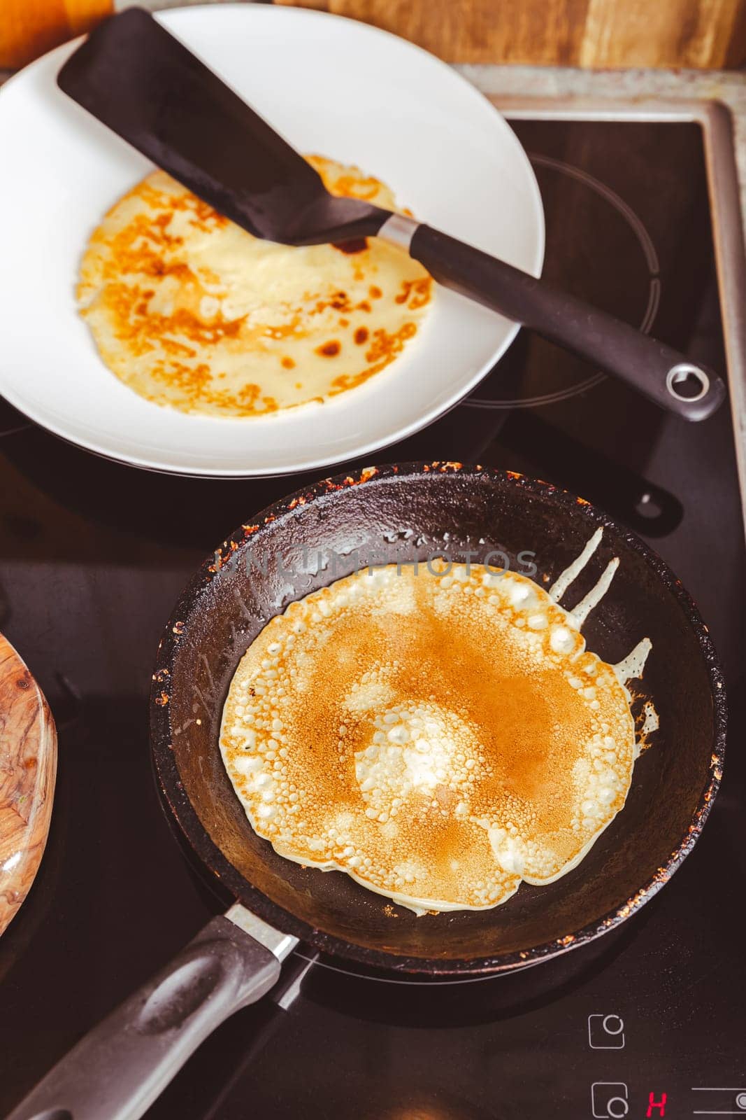 Making thin pancakes on frying pan in kitchen, with cooking dough for crepes and pancakes.
