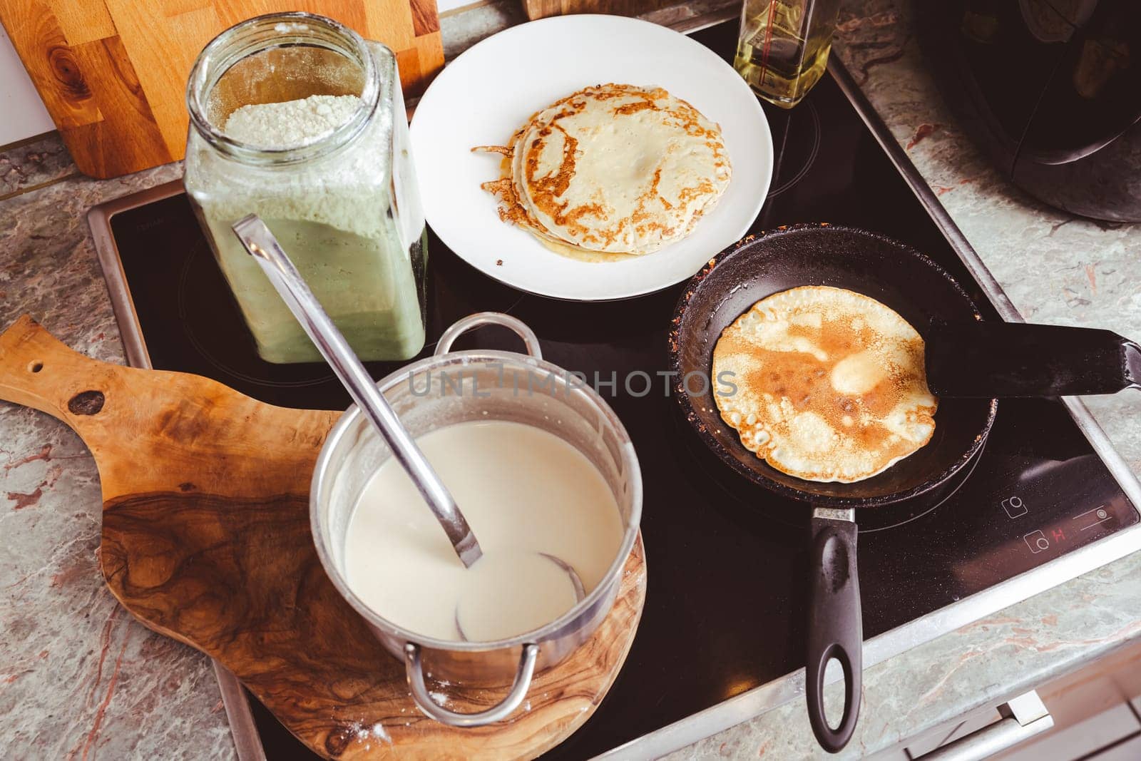 Making thin pancakes on frying pan in kitchen, with cooking dough for crepes and pancakes.