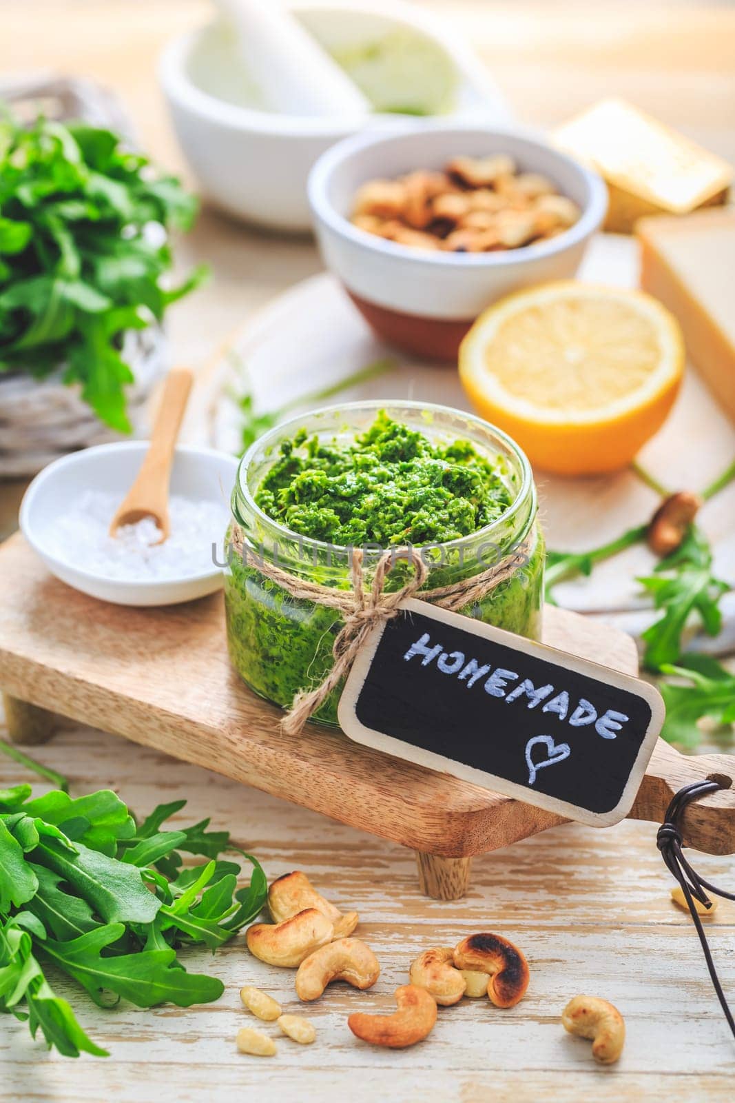Homemade arugula pesto with ingredients on wooden background