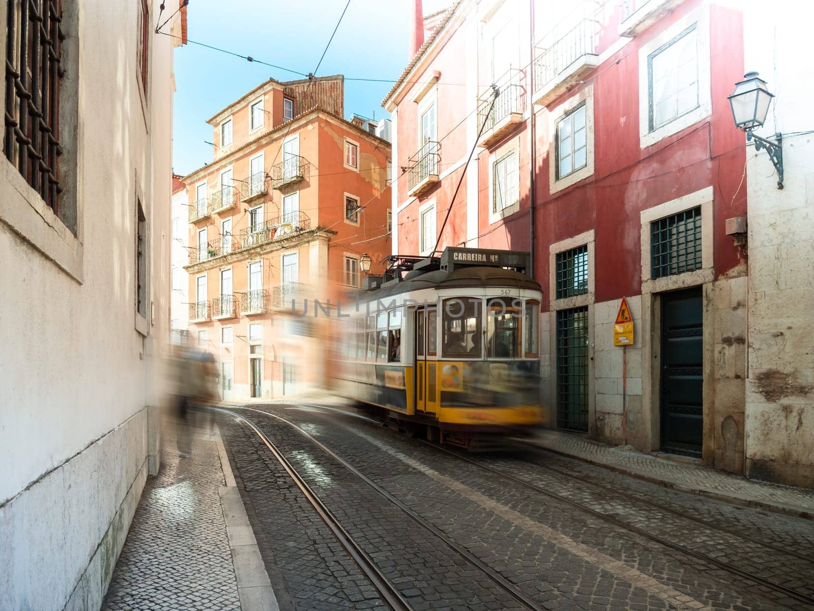 Lisbon tram with yellow color driving fast in a small street in the centre of the city during sunrise
