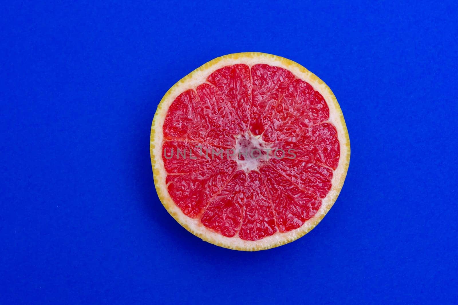 Sliced side of a grapefruit with red pulp isolated on a blue background