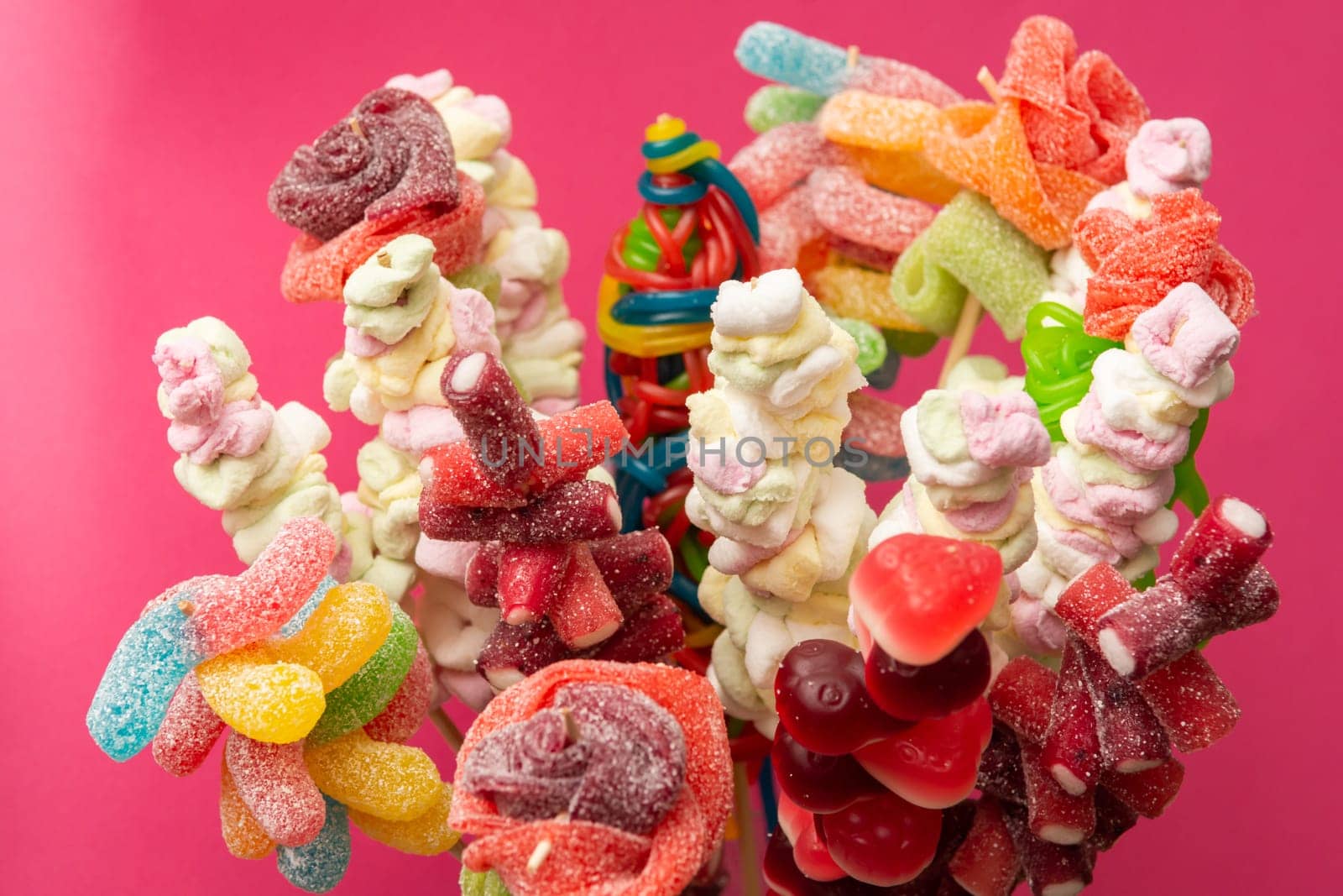 Variation of colorful fruit gums sweets skewered sour gummy bears marshmallow on wooden skewers isolated on a magenta red background