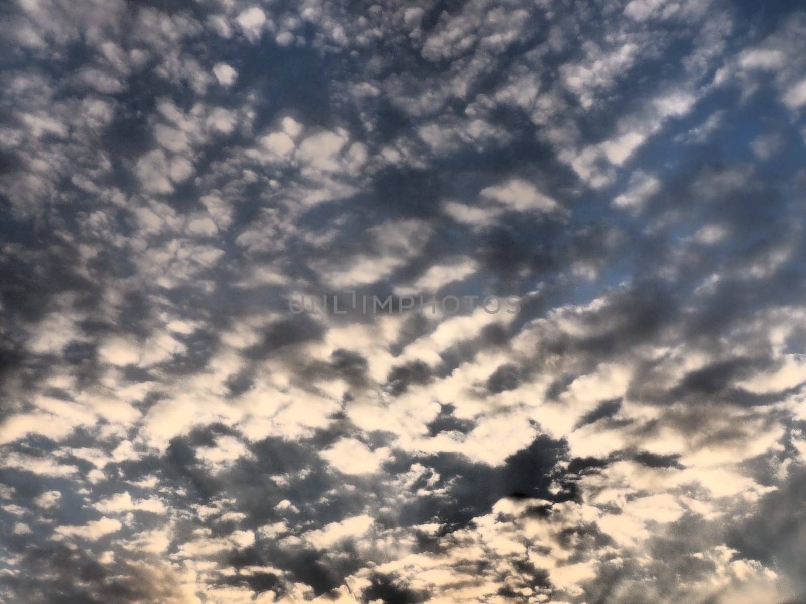 Clouds in the evening sky. The sun's rays pierce the clouds. Blue, yellow and orange colors of the sky and clouds. Beautiful landscape. The sun goes down.