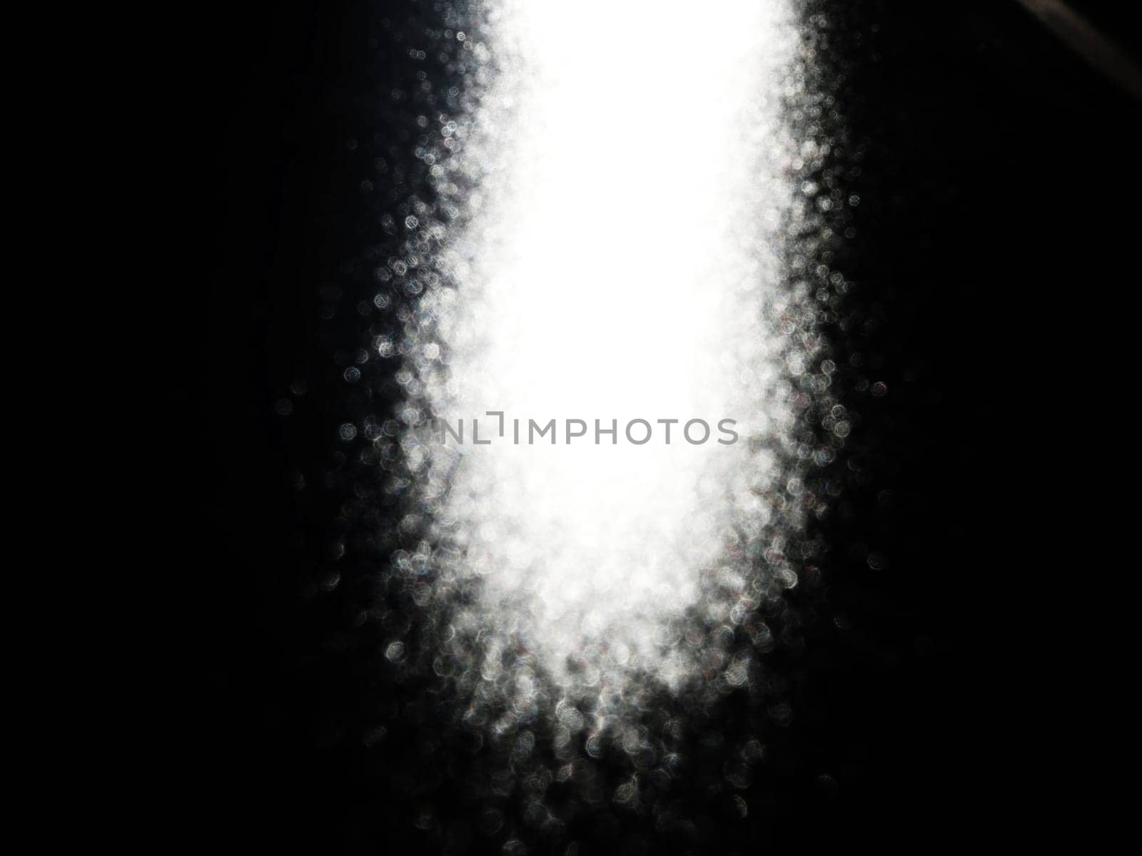 White bokeh and beam on a black background. Blurred glow from above on a dark surface. Night or space theme. Bokeh for the holiday. Association for a flying meteorite. Abstract theme.