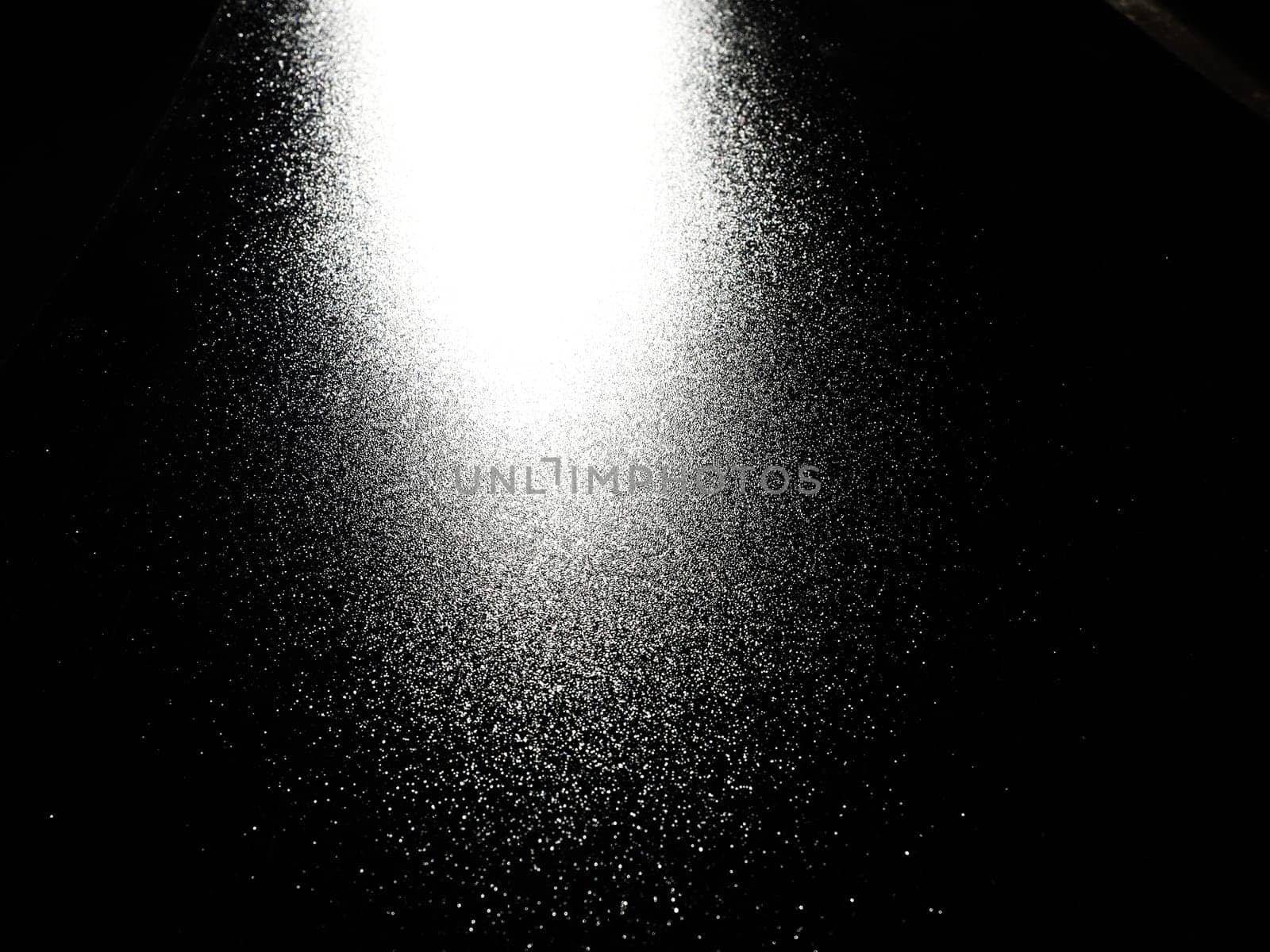 White bokeh and beam on a black background. Blurred glow from above on a dark surface. Night or space theme. Bokeh for the holiday. Abstract background. Glare, ray and light shine from above.