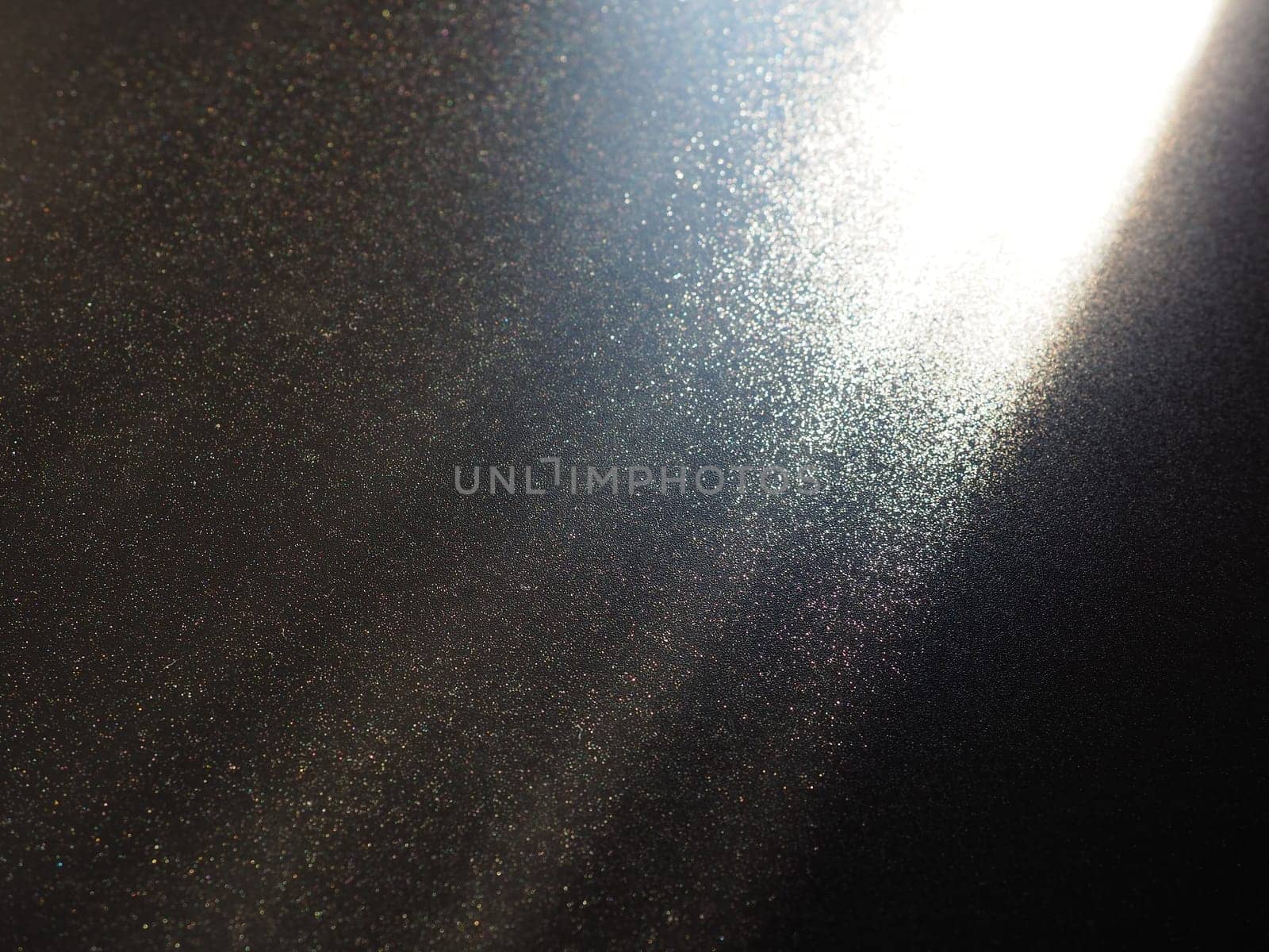 Abstract black background. Oblique light rays on a black blackdrop with flickering dots. From right top, the lines are directed down and to the left. Glow, flare or shine. Side lighting. Small glow.