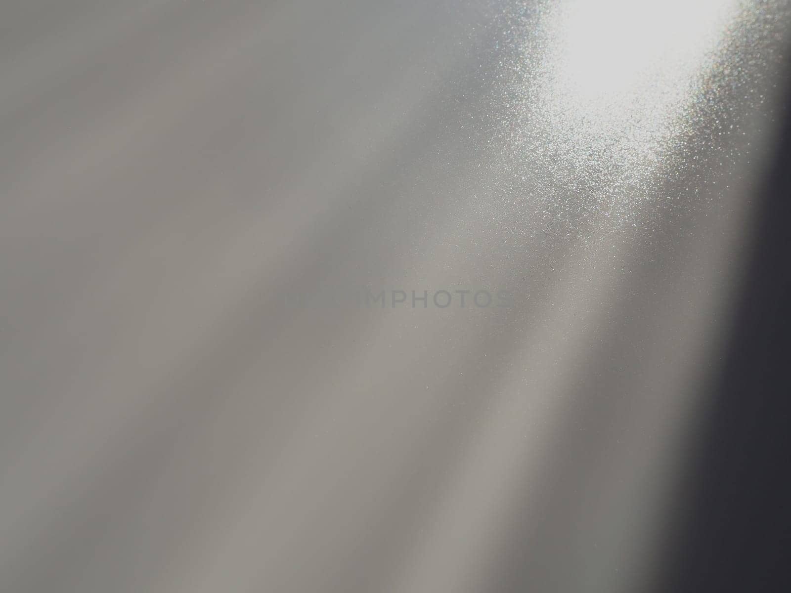 Diagonal rays of light on a gray background. Blurred abstract background light effect, light leaks. Side surface illumination. Small sparks and glow. Shine, glint or glare. Right top left down.