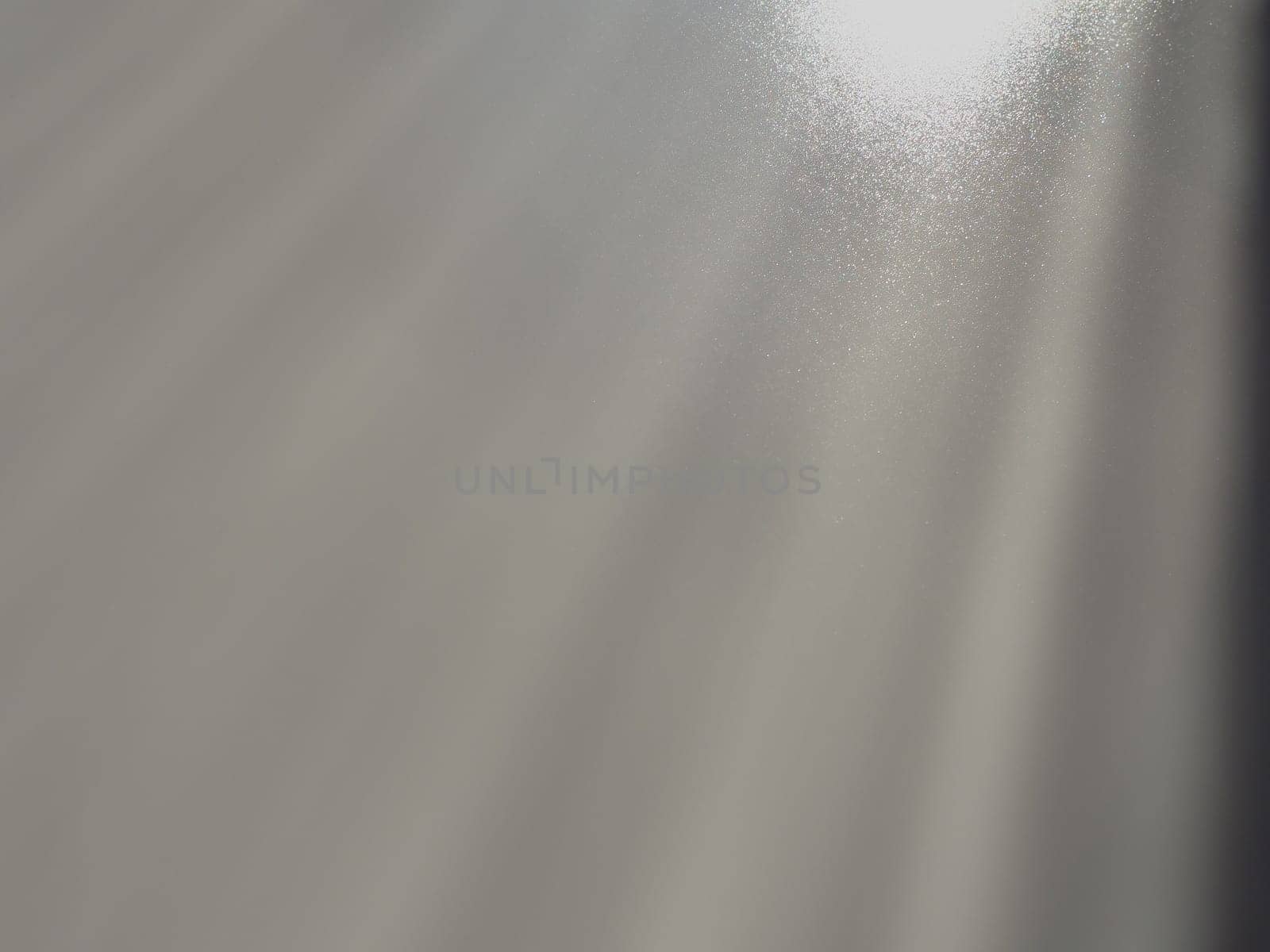 Diagonal rays of light on a gray background. Blurred abstract background light effect, light leaks. Side surface illumination. Small sparks and glow. Shine, glint or glare. Right top left down.