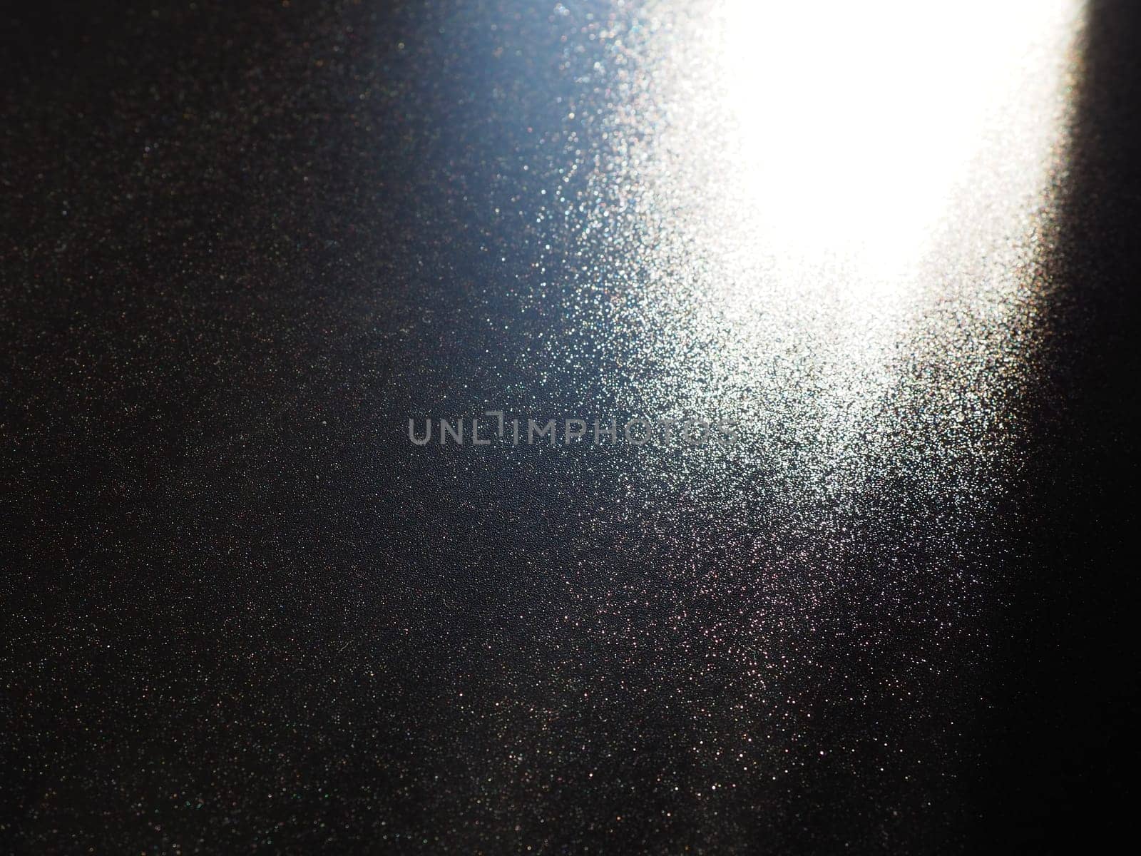 Abstract black background. Oblique light rays on a black blackdrop with flickering dots. From right top, the lines are directed down and to the left. Glow, flare or shine. Side lighting. Small glow.