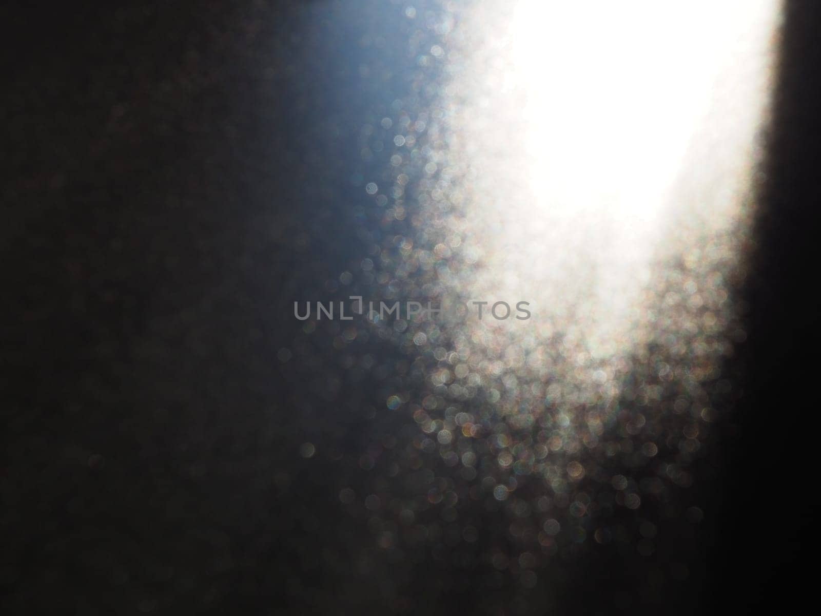 White bokeh and beam on a black background. Blurred glow from above on a dark surface. Night or space theme. Bokeh for the holiday. Association for a flying meteorite. Abstract theme.