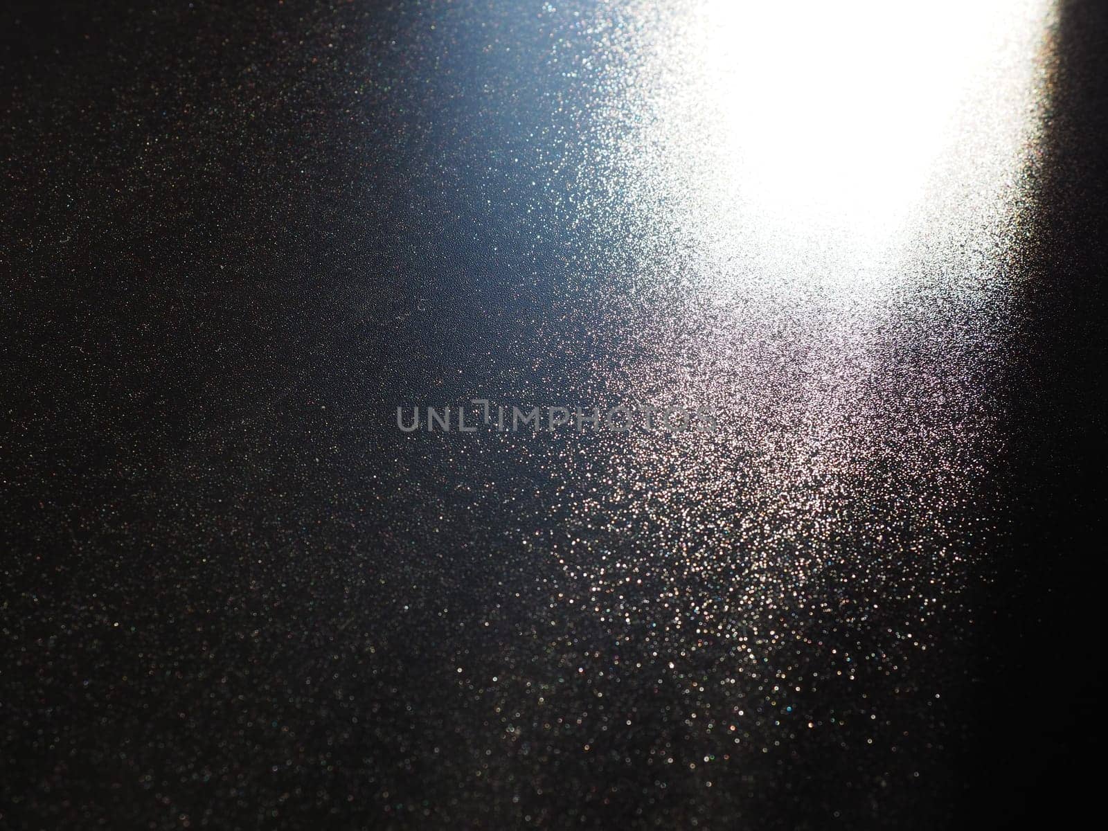 Abstract black background. Oblique light rays on a black blackdrop with flickering dots. From right top, the lines are directed down and to the left. Glow, flare or shine. Side lighting. Small glow.