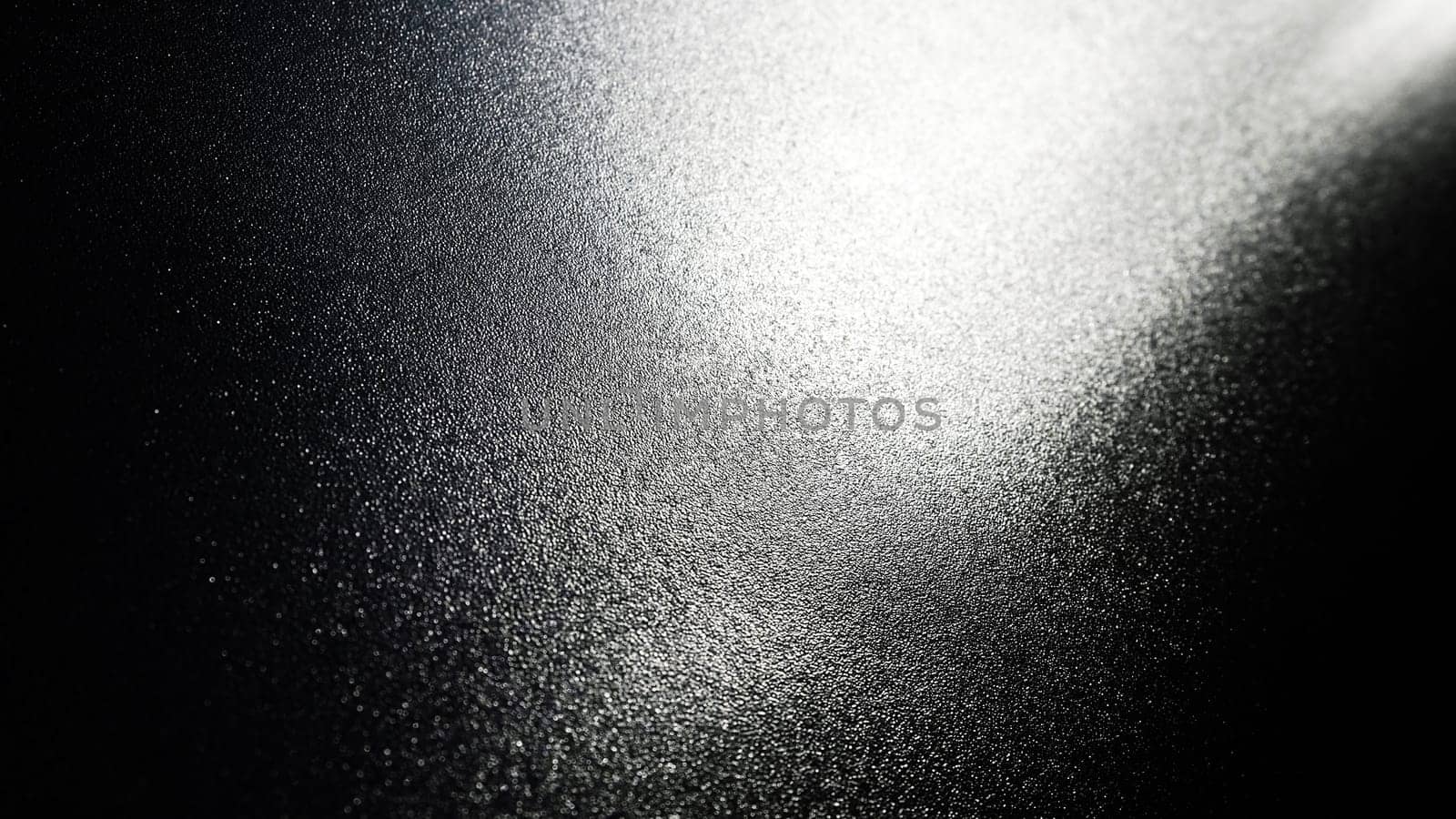 White bokeh and beam on a black background. Blurred glow from above on a dark surface. Night or space theme. Bokeh for the holiday. Abstract background. Glare, ray and light shine from above.