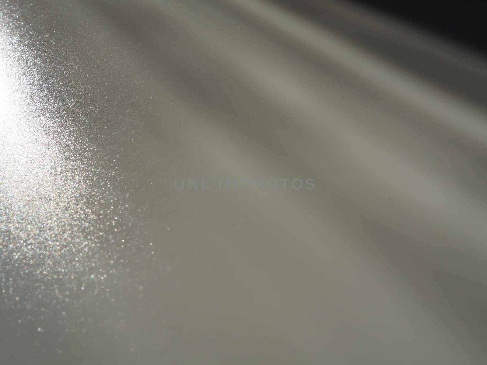 Diagonal rays of light on a gray background. Blurred abstract background light effect, light leaks. Side surface illumination. Small sparks and glow. Shine, glint or glare. Left top right down