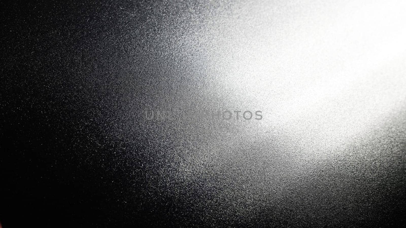 White bokeh and beam on a black background. Blurred glow from above on a dark surface. Night or space theme. Bokeh for the holiday. Abstract background. Glare, ray and light shine from above.