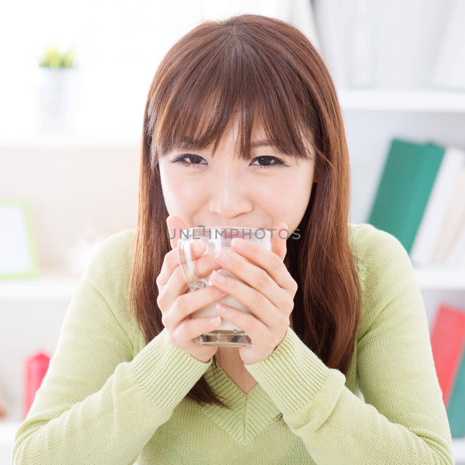 Portrait of happy Asian girl drinking soymilk as breakfast. Young woman indoors living lifestyle at home.