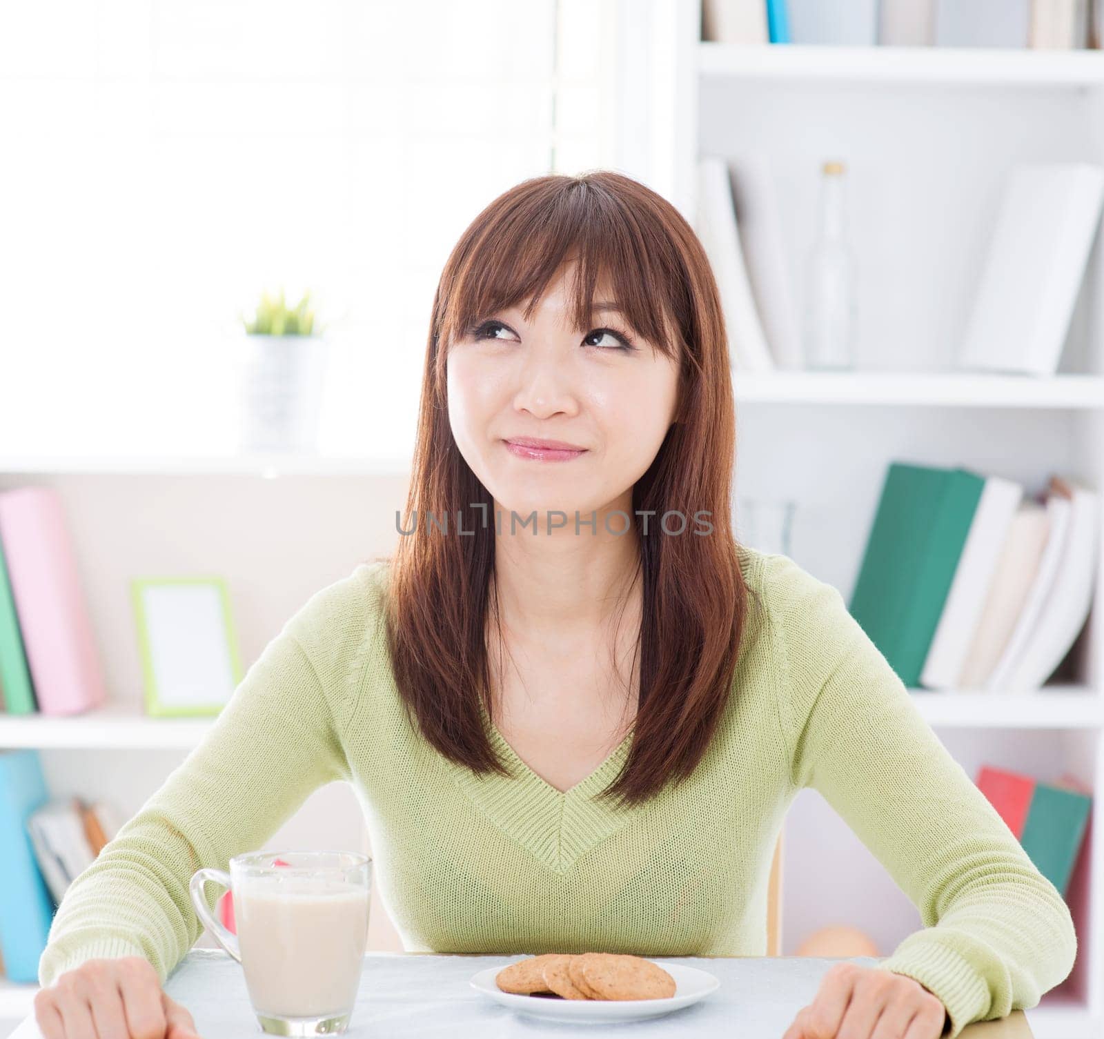 Portrait of happy Asian girl thinking and smiling while having breakfast. Young woman indoors living lifestyle at home.