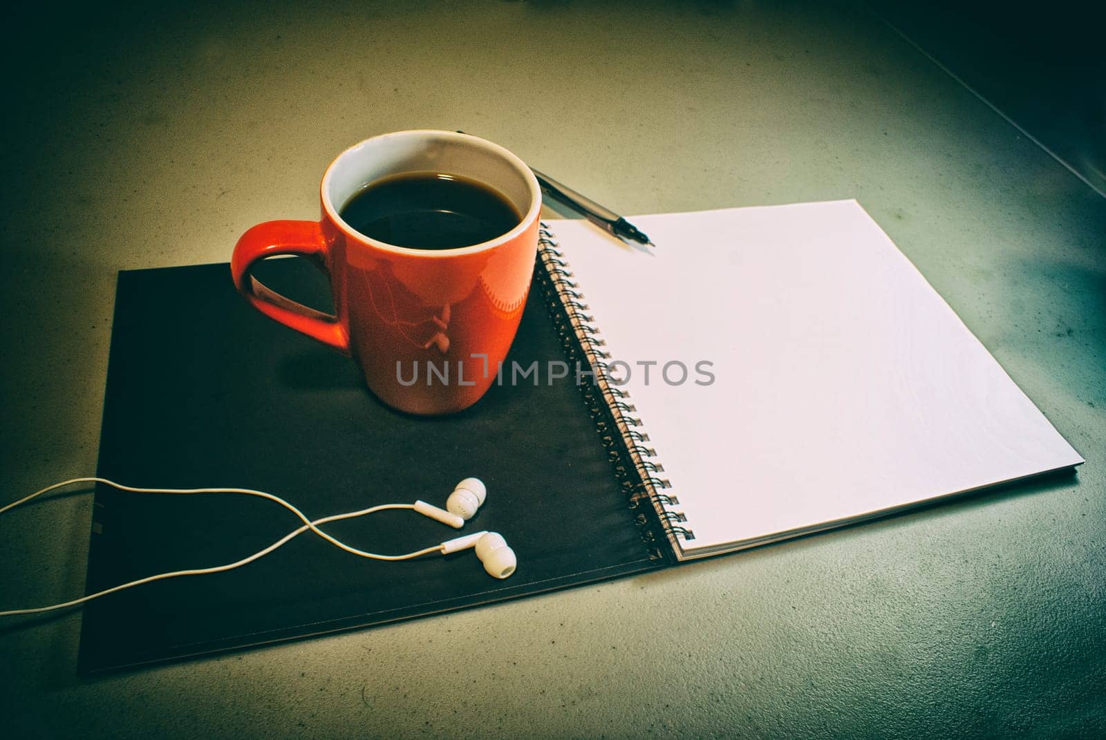Photograph of an open notebook, a cup of coffee, a pen and a pair of earphones in a grunge style and grainy look