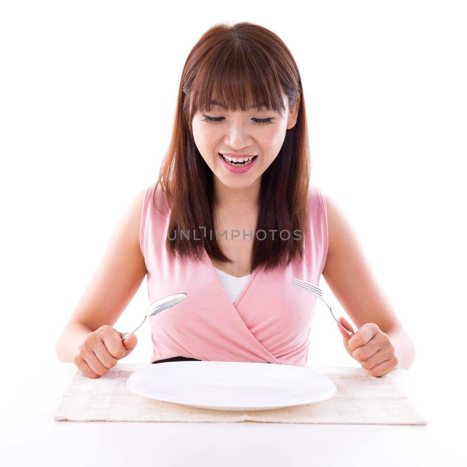 Asian girl holding fork and spoon with surprised expression, empty plate ready for food. Young woman living lifestyle.