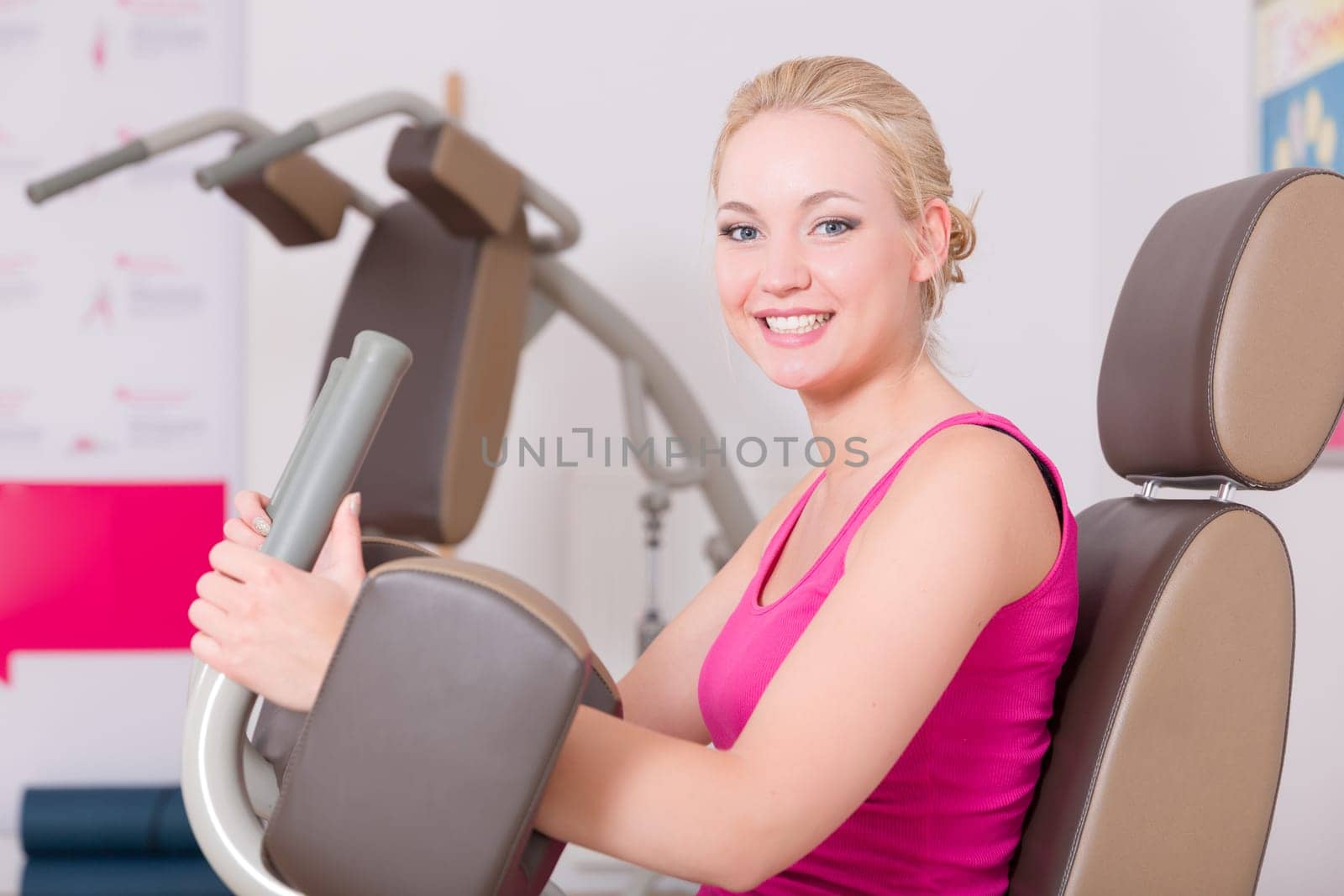 A young pretty woman in a pink shirt doing exercises in a gym