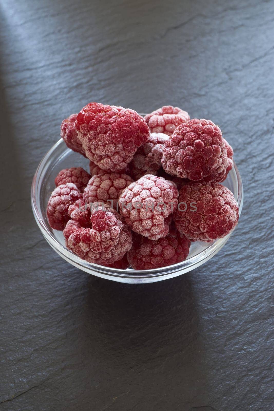 Frozen raspberries in a glass bowl on slate slab